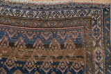 Geometric boteh motifs and abrashed blue-brown ground on antique Kurdish rug with even wear.