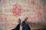 Distressed vintage Oushak rug showcasing its worn pile, pale cochineal red, ivory, and mint green motifs.