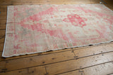 Distressed Oushak rug edge displaying muted red, ivory tones, and visible foundation.