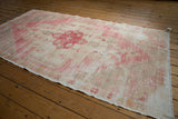 Distressed Oushak rug corner, faded cherry red and sand, visible wear, checkered patterns.
