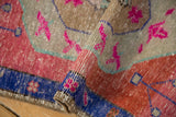 Curled edge of distressed Oushak rug, intact selvage, royal blue border, pink floral motifs.