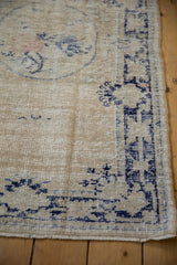 Distressed Oushak rug corner, faded ivory field, navy geometric border, low pile, fringe.
