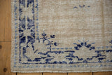 Distressed Oushak rug corner close-up, showing faded navy border, ivory field, and fringe.