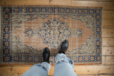 Distressed Oushak rug with apricot grid panel, faded midnight blue floral patterns, and even wear.