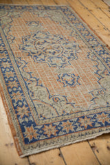Detail of distressed Oushak rug: worn apricot, ivory pile, faded blue grid pattern, foundation visible.