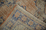 Distressed Oushak rug texture, showing apricot, faded blue, ivory geometric patterns and wear.