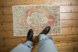 Distressed Oushak rug showing blush, seafoam green, ivory floral medallion with textural pile wear.