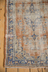 Distressed Oushak rug corner with worn pile, intact selvage, and blue geometric border.