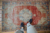 Corner detail of distressed vintage Oushak rug, showing faded red, pale blue motifs, and low pile.