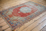 Corner of vintage distressed Oushak rug, showing faded red and blue border pattern and wear to foundation.