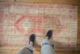 Distressed vintage Oushak rug with faded raspberry red geometric medallions and visible wear.