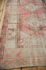 Angled close-up of distressed pink and sand geometric Oushak rug with intact side selvage.