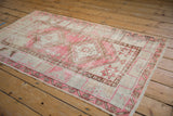 Distressed pink and beige vintage Oushak rug corner, featuring geometric patterns and softened texture.