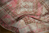 Distressed vintage Oushak rug texture with blush pink, sand, and brown geometric motifs.