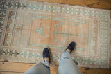 Distressed Oushak runner with faded prayer design, dusty sand, muted green, and feet.