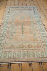 Angled view of distressed vintage Oushak prayer rug, with faded plum and green tree-of-life motif.