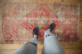 Distressed vintage Oushak rug featuring faded red multi-medallions with visible hand-knotted texture.