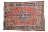 Distressed Oushak rug with faded red field, scalloped blue medallion, and ivory floral vinery.