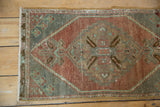 Distressed Oushak rug corner showing woven texture, aubergine, slate, mint green tones and fringe.