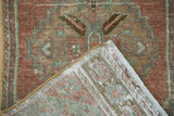 Distressed vintage Oushak rug corner, showing mostly even pile wear, hand-knotted foundation, and fringed edge.