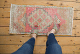 Distressed Oushak rug mat with muted pink, beige, and teal pattern, highlighting texture underfoot.
