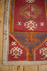 Distressed Jijim rug corner with wine red geometric gul, orange plant, dusty violet spandrel.