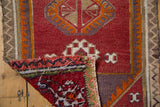 Distressed Jijim rug showing wine red geometric guls, with corner exposing textured reverse.