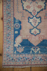 Vintage distressed Oushak rug corner with pale sapphire blue and dusty rose floral motifs.