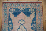 Distressed Oushak rug's pearl adorned field and pinwheel floral border in pale rose, ivory, and blue.