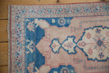 Vintage Oushak rug corner showing softened rose field, blue border, and fringe detail.