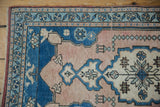 Distressed Oushak rug corner, showcasing pale sapphire blue, dusty rose, and ivory floral border patterns.