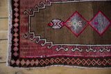 Distressed Oushak rug corner, showing burgundy field, charcoal border, and diamond, hook motifs.