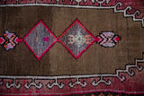 Distressed brown field with bright pink diamond patterns and stylized burgundy border on an Oushak rug.