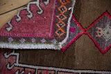 Distressed vintage Oushak rug pile texture showing burgundy, brown, and bright pink edge.