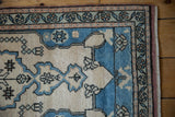 Distressed Oushak rug corner: ivory main field, sapphire blue medallion, peach and seafoam floral borders.