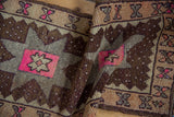 Distressed Oushak rug detail showing textured brown pile and vivid pink starburst motif.