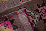 Textured fold of a distressed Oushak rug, showing vibrant pink edge and geometric patterns.