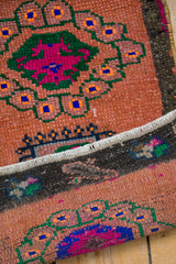 Vibrant pink, green, and blue floral motifs on the distressed sandalwood pile with white fringe.