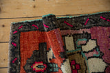 Rolled edge of a hand-knotted distressed Oushak rug in fuschia, rust, and turquoise.