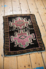 Angled view of a distressed Oushak mat with its weaver inscription and geometric mauve medallion.