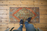Distressed Oushak mat with geometric stepped patterns in faded rust, blue, and green.