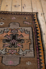 Close-up of distressed vintage Oushak rug shows geometric border in charcoal, saffron, and pink.