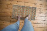 Distressed vintage Oushak mat with geometric floral patterns in sandalwood and silver tones, showing wear.