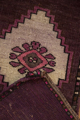Distressed Oushak rug corner revealing stepped aubergine and ivory pattern with numbered reverse.