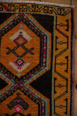 Distressed Oushak rug corner showing geometric saffron, charcoal, pink patterns and purple selvage.