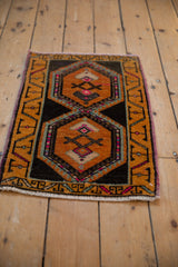 Distressed vintage Oushak rug mat corner with saffron, charcoal, and pink geometric pattern.
