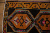 Distressed Oushak rug close-up: geometric pattern in saffron, charcoal, and vibrant pink.