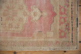 Distressed pink and beige Oushak rug, showing even wear, curvilinear pattern, and side selvage.