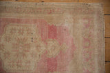 Distressed Oushak rug pile close-up: blush, pink, and sand tones with knot wear.