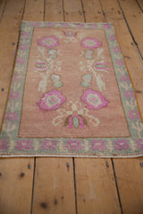 Distressed pile texture of dusty rose Oushak rug, with pink blossoms and green border.
